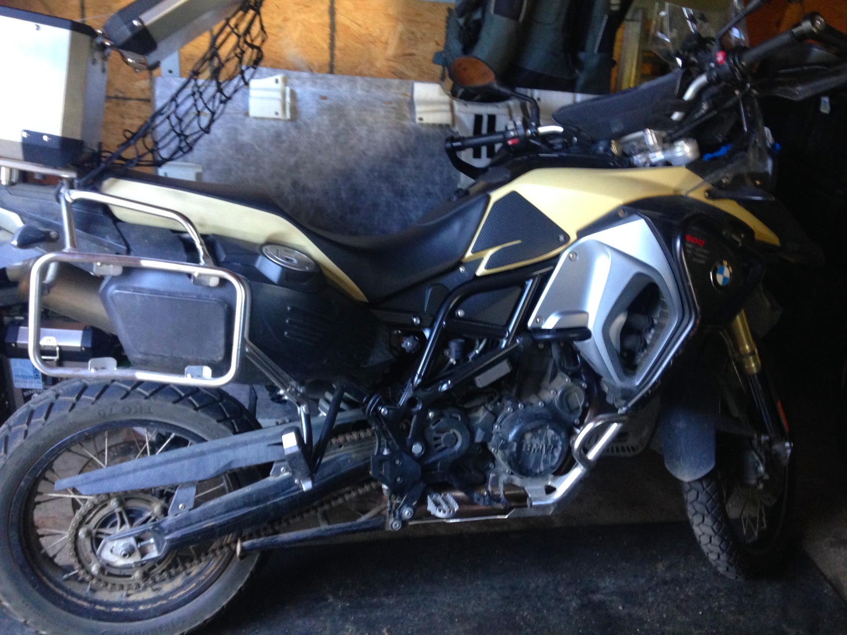 A sand-coloured BMW F 800 Adventure in a shed with racks and a cargo net