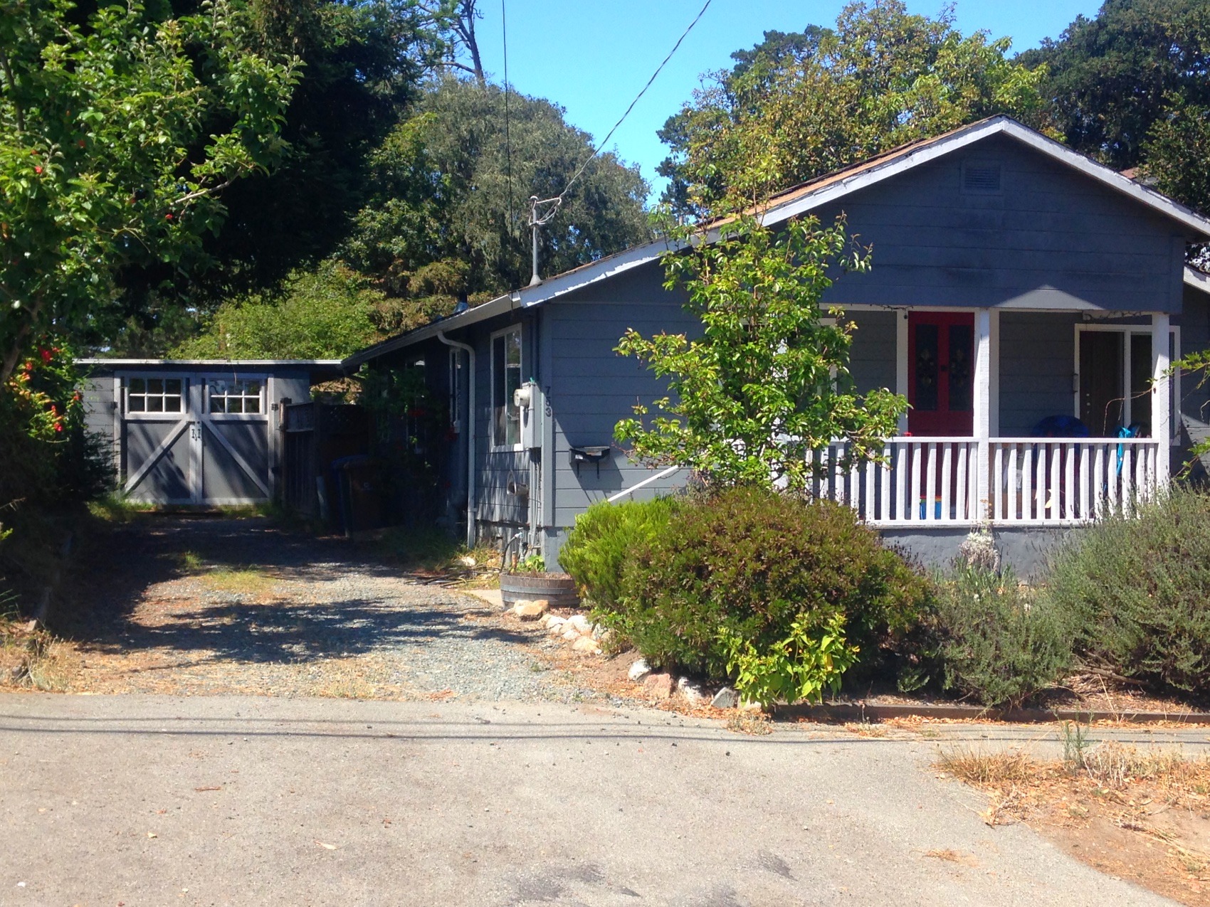 A blue-grey timber house with a red door and a dirt drive