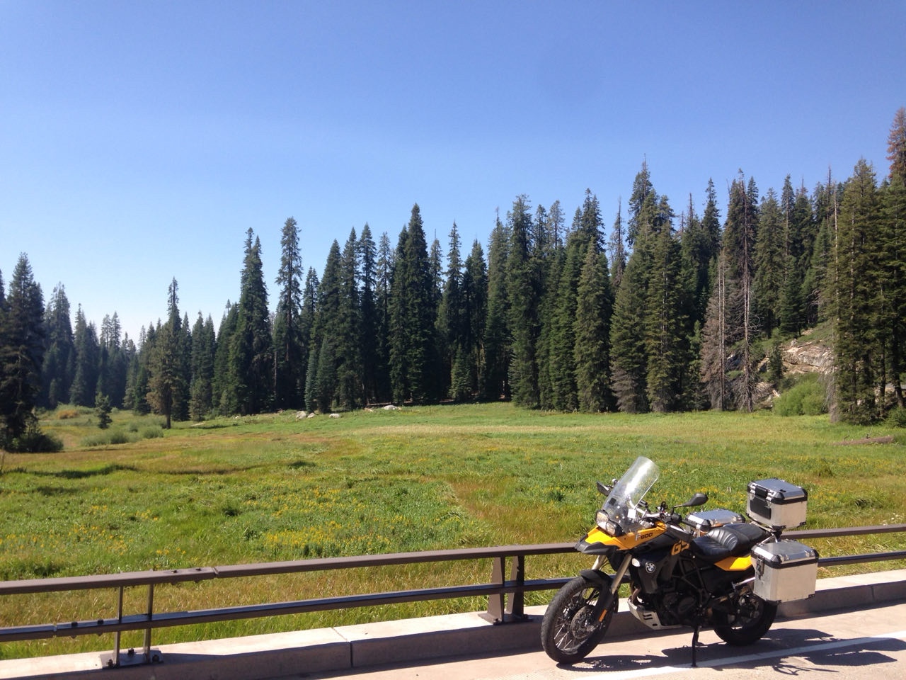 The motorcycle at a guardrail above a green mountain meadow