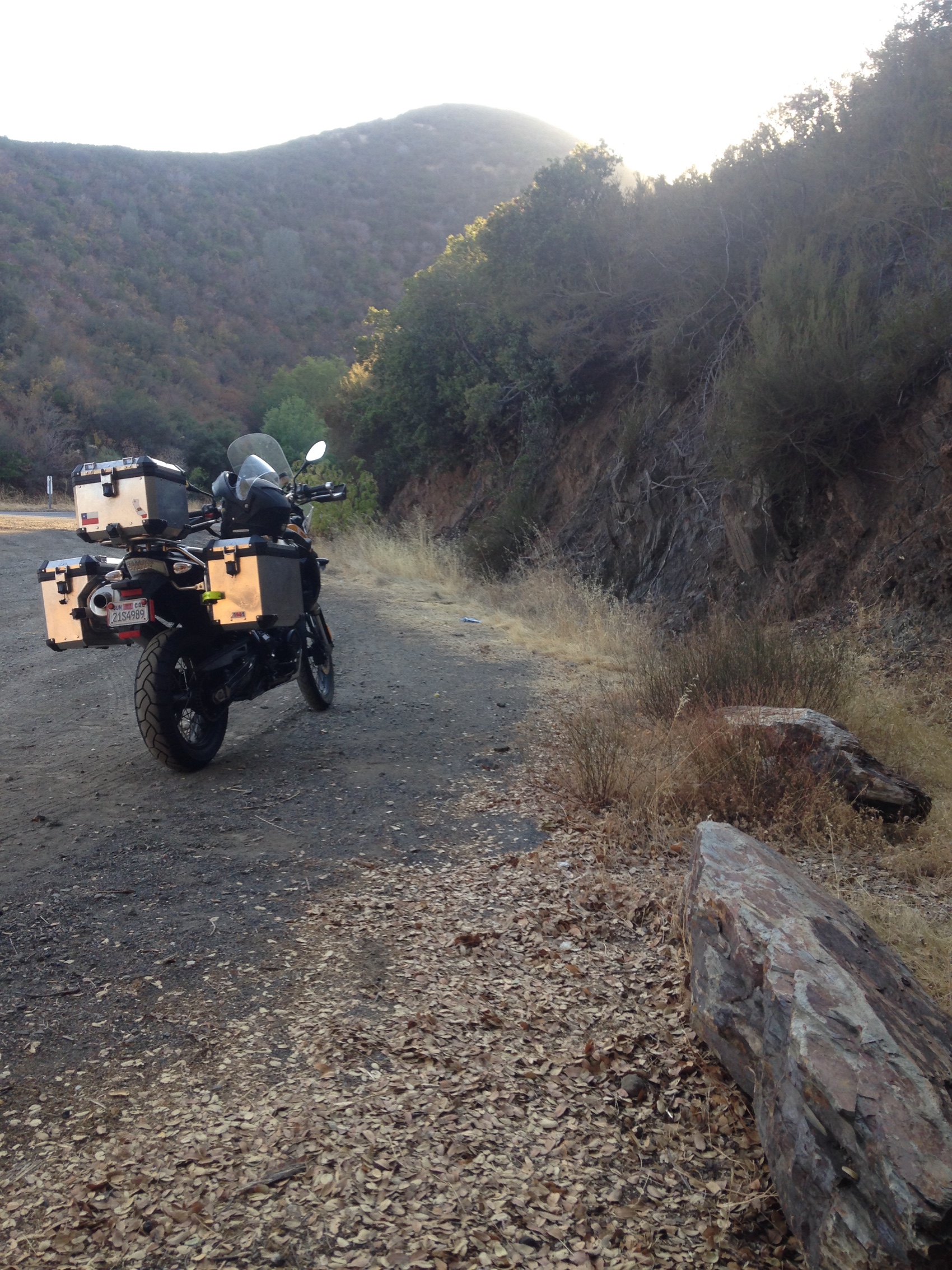 The motorcycle on a dirt road cut into a dry hillside at low sun
