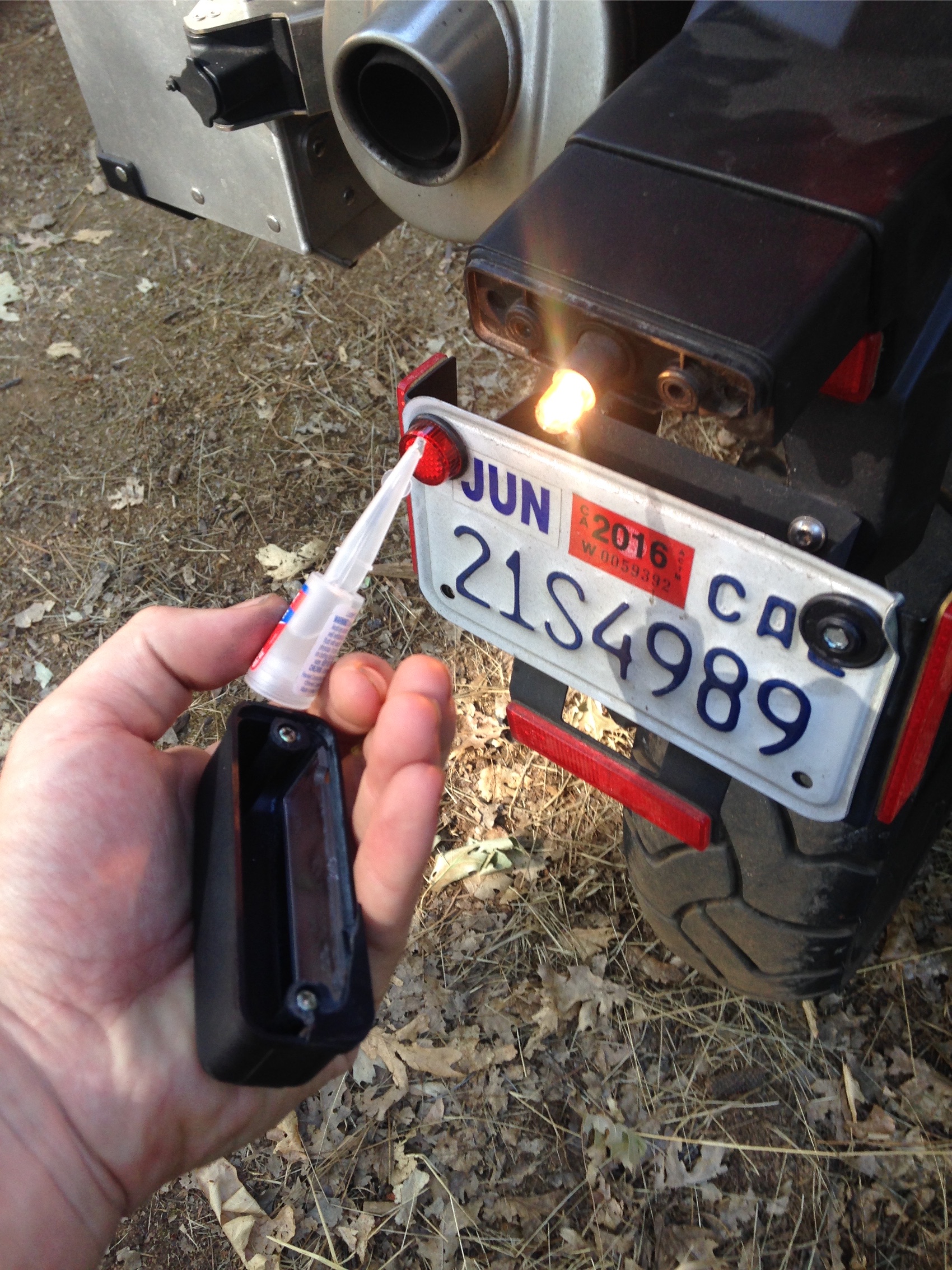 A hand gluing the broken number plate light of the motorcycle