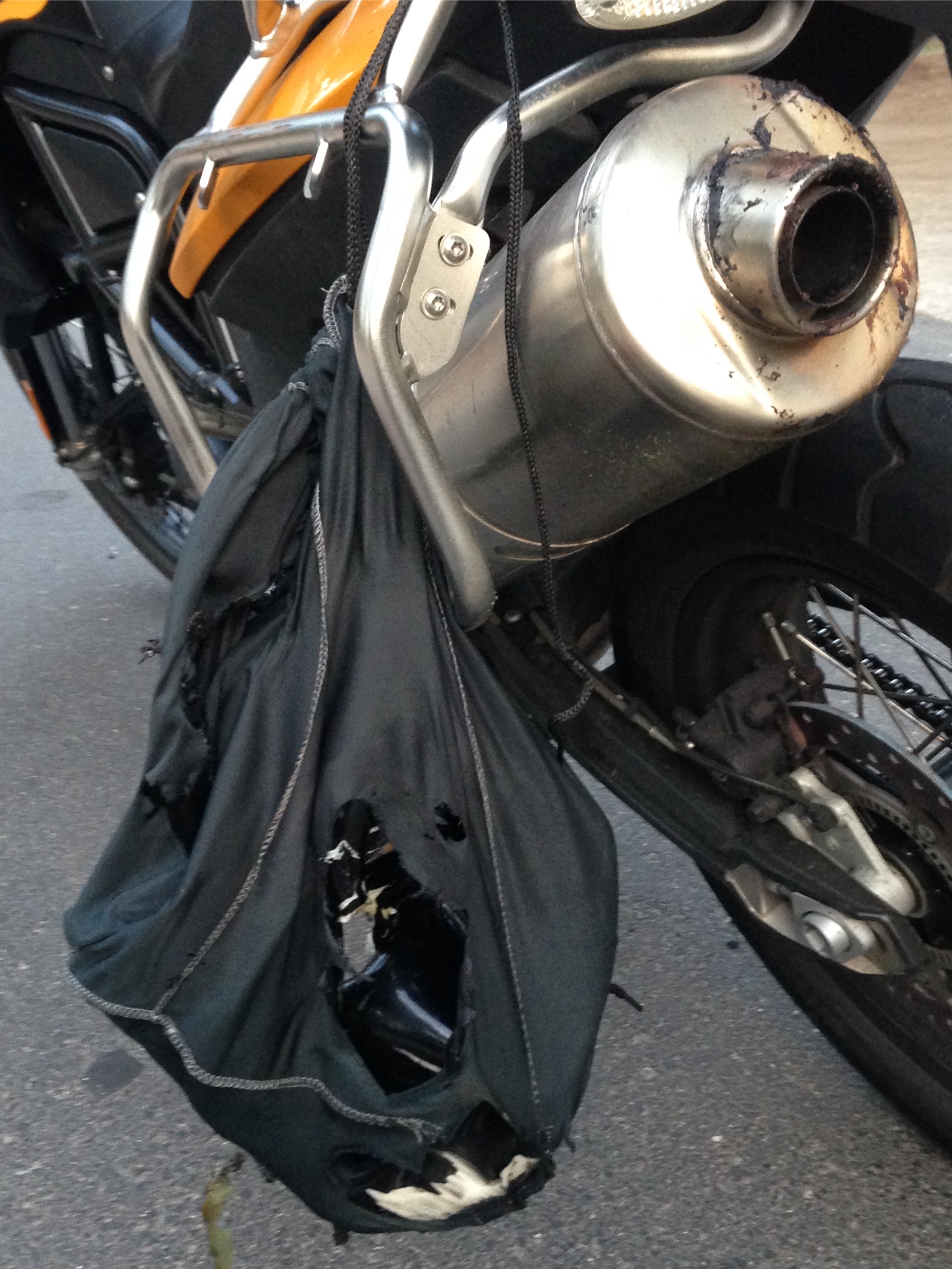 A burnt bag hanging off the motorcycle exhaust with holes melted through it