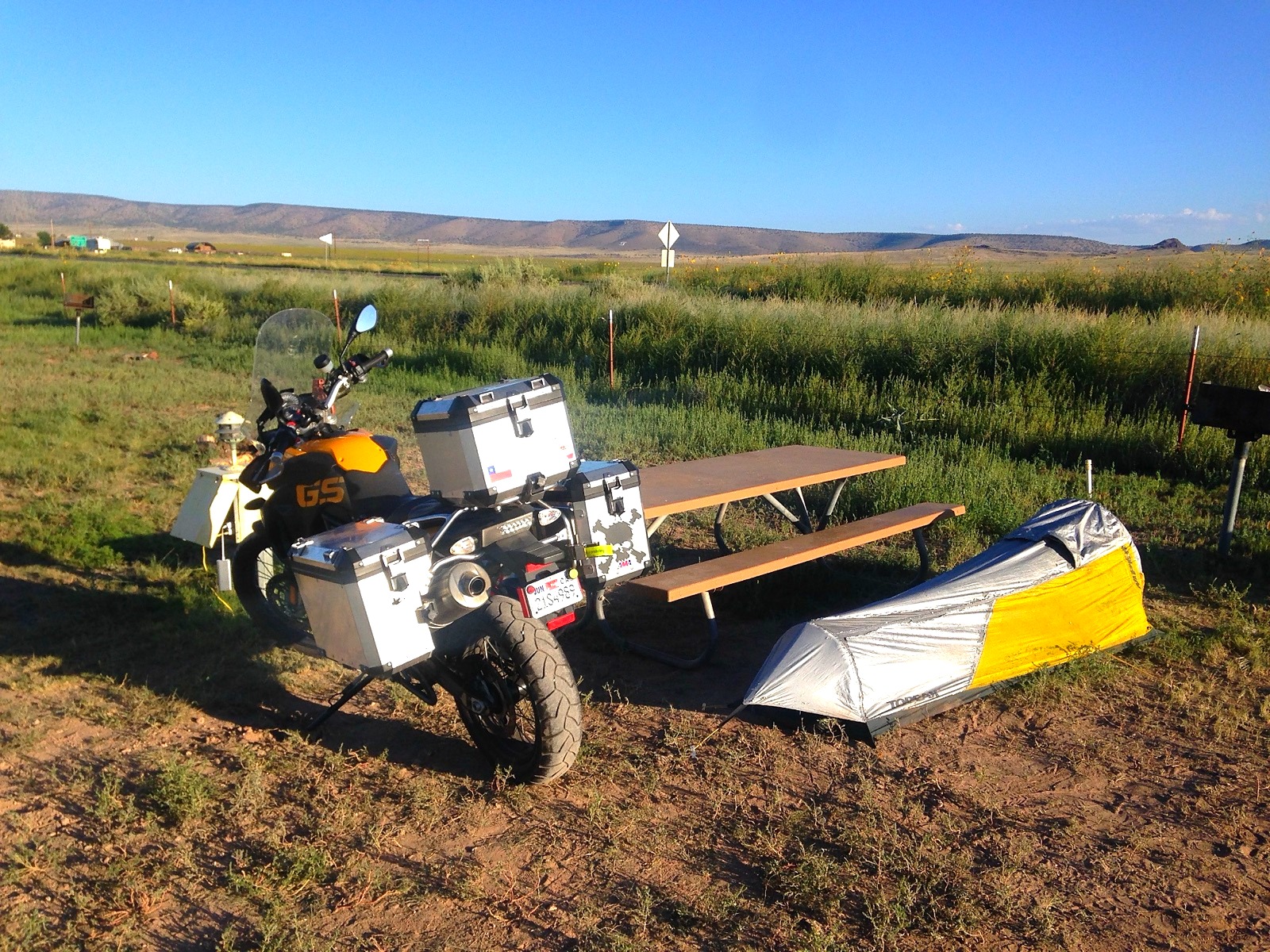 The motorcycle and a bivvy beside a picnic table in a field