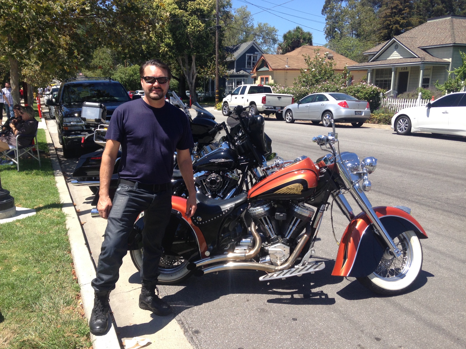 Randy standing beside his Indian in a street lined with Harleys