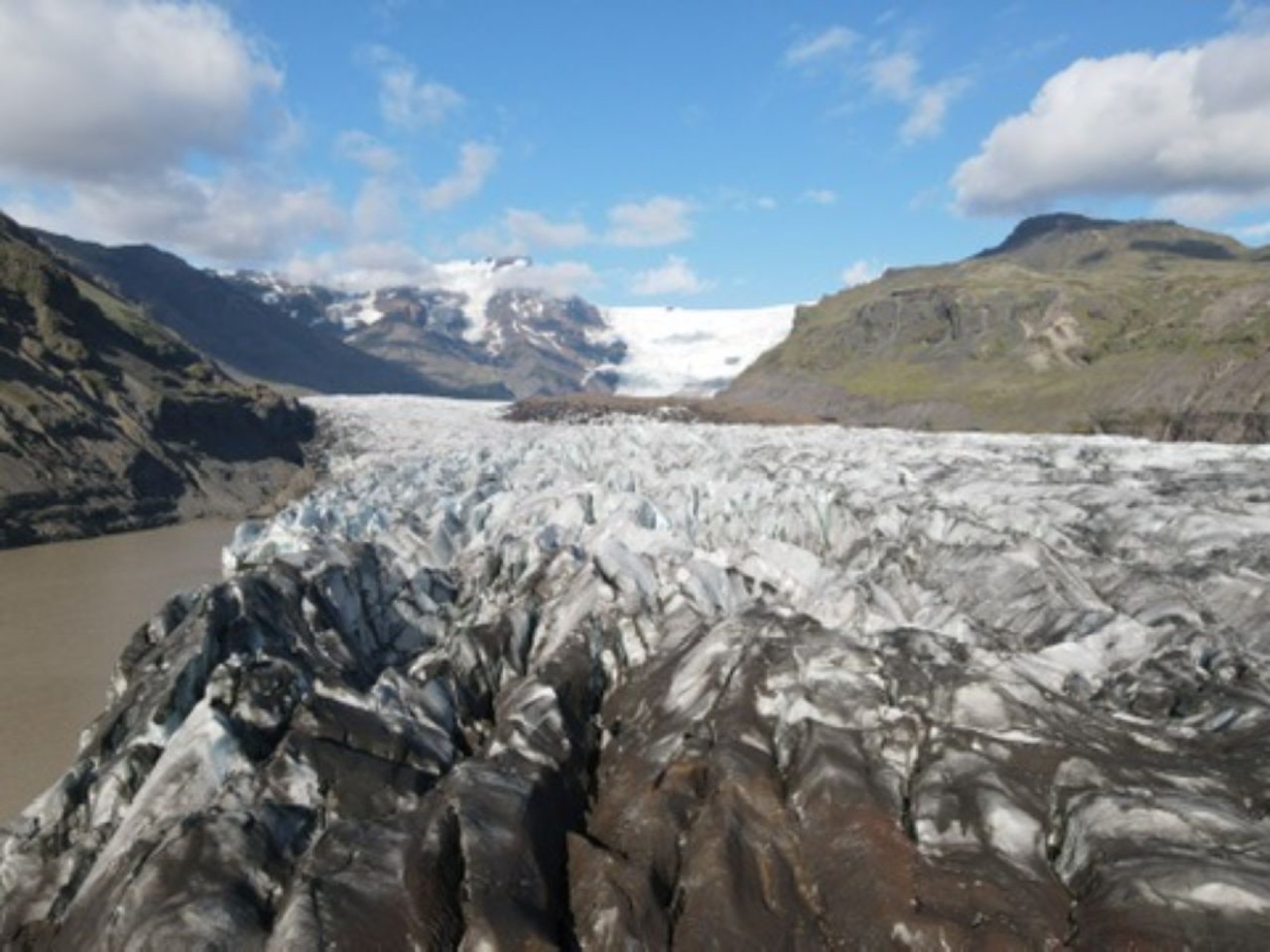 The cracked grey surface of a glacier running down between mountains