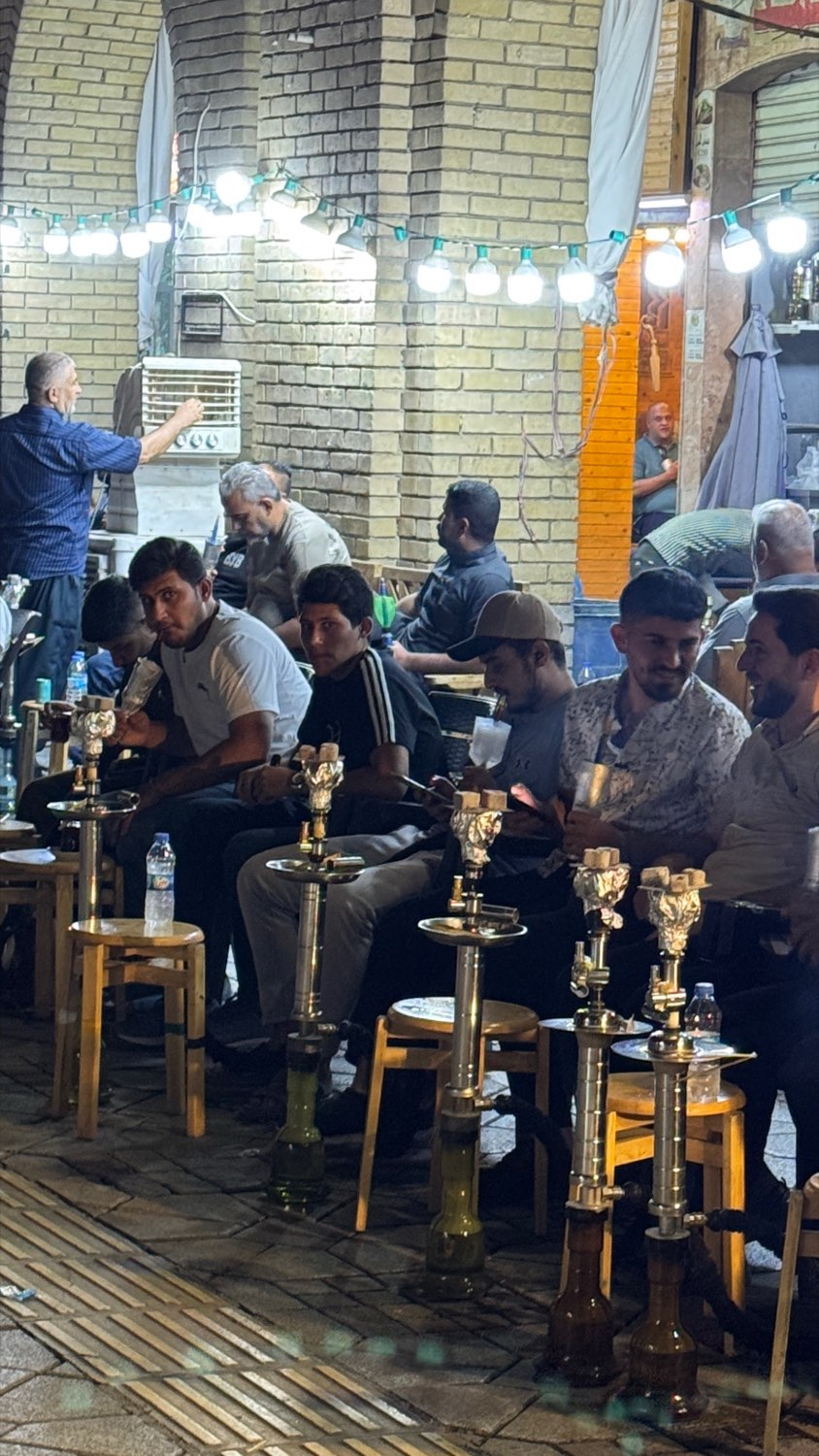 Men sitting with shisha pipes under strung lights in a night tea house