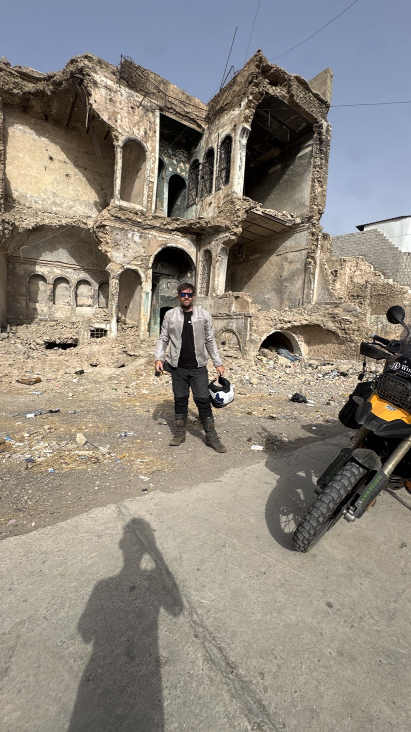 Rodrigo standing with his helmet in front of a gutted building in Mosul
