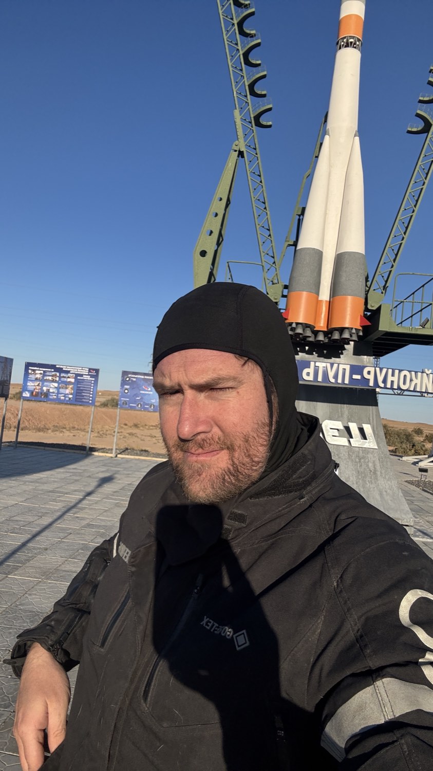 Rodrigo in a beanie in front of the rocket monument, squinting into the cold sun