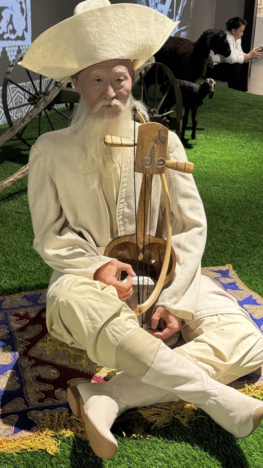 A figure in a museum diorama playing a stringed instrument inside a yurt
