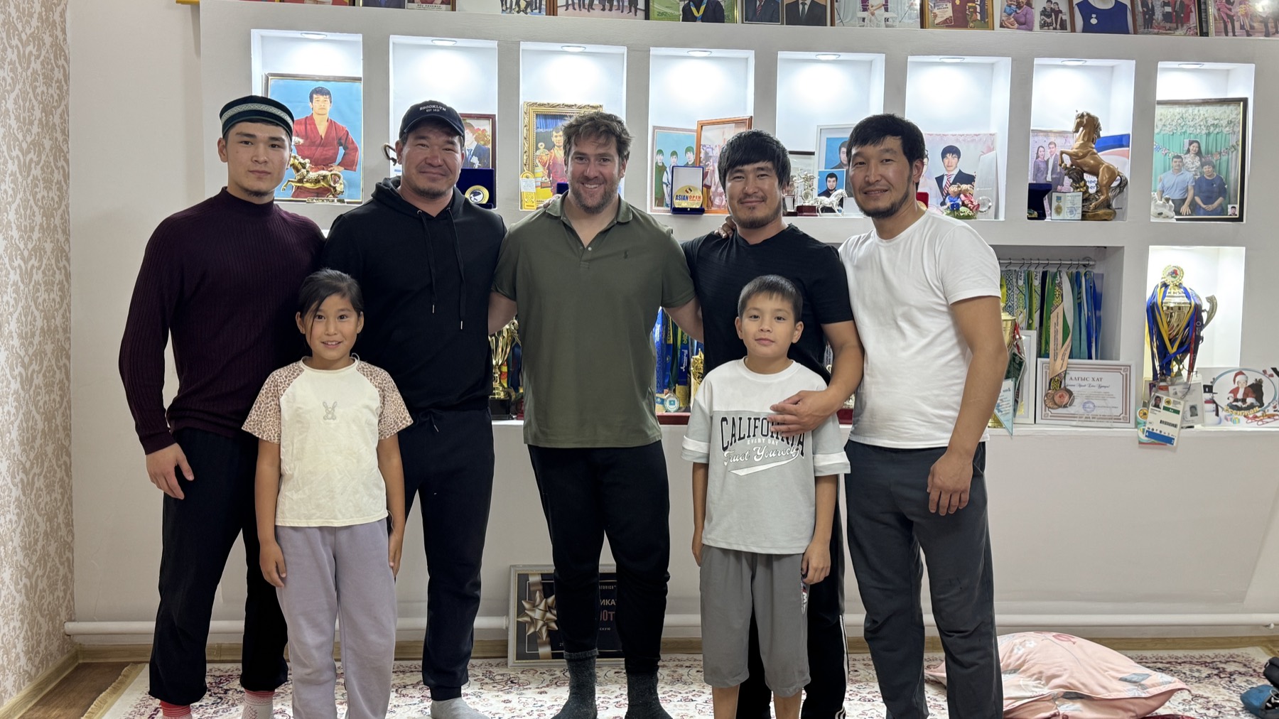 Rodrigo with a Kazakh family in a room lined with wrestling trophies