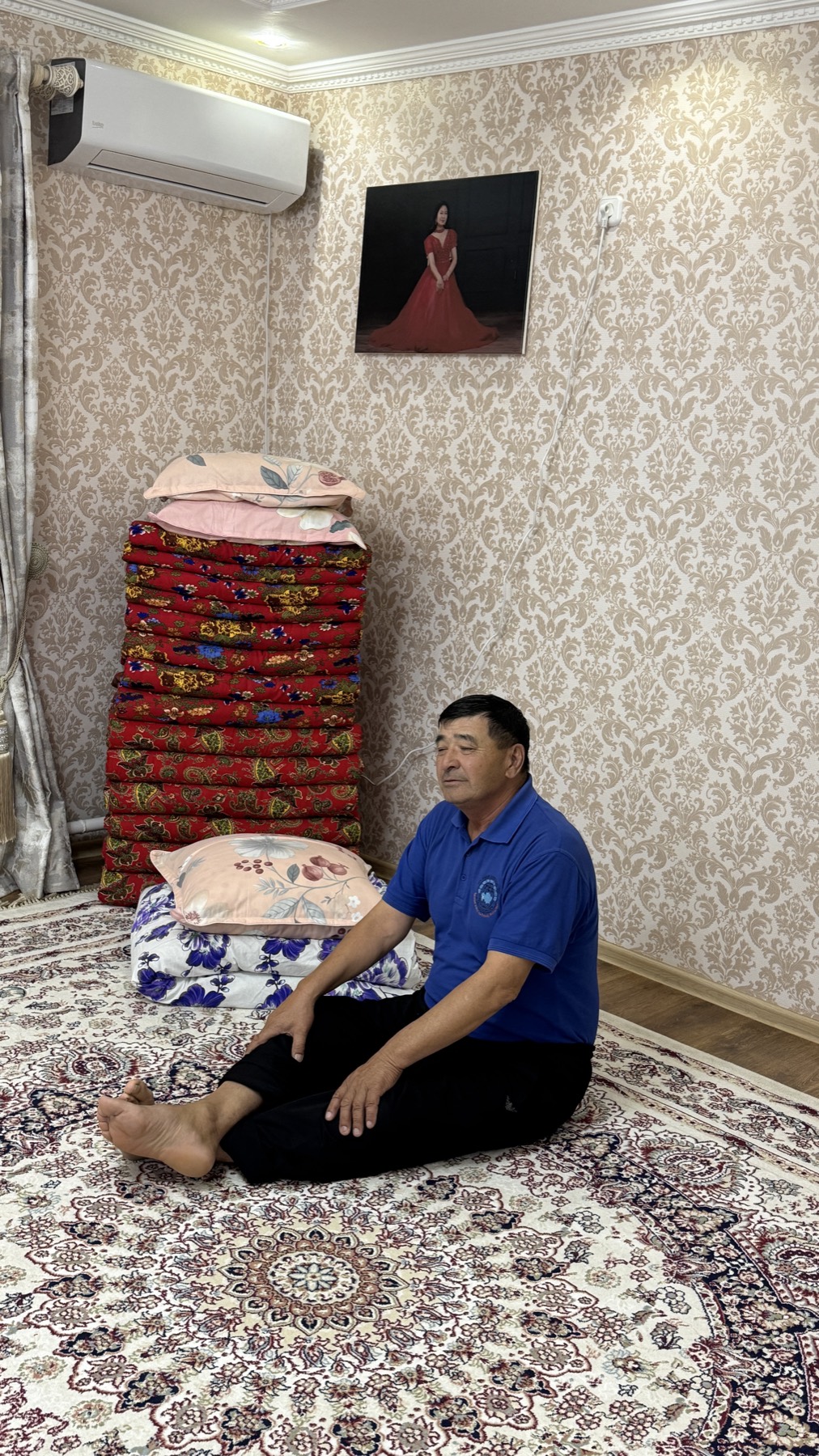 A Kazakh man sitting on the carpet beside a stack of quilts