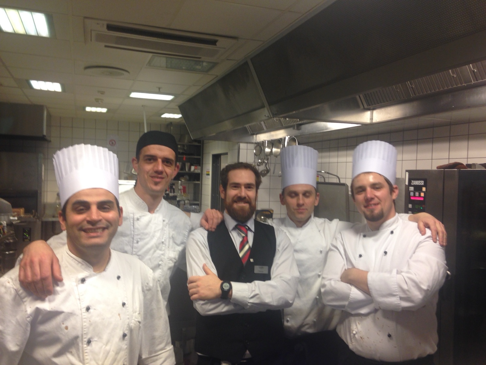Rodrigo in waistcoat and tie with his arms around five cooks in white