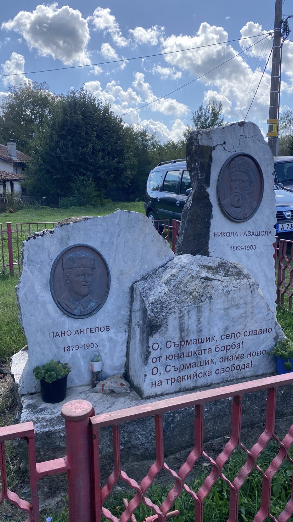 A stone monument to two Bulgarian revolutionaries behind a red railing in a village