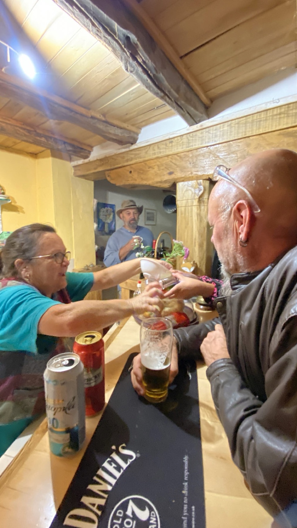 A woman pouring beer behind a wooden bar with two men leaning on the counter