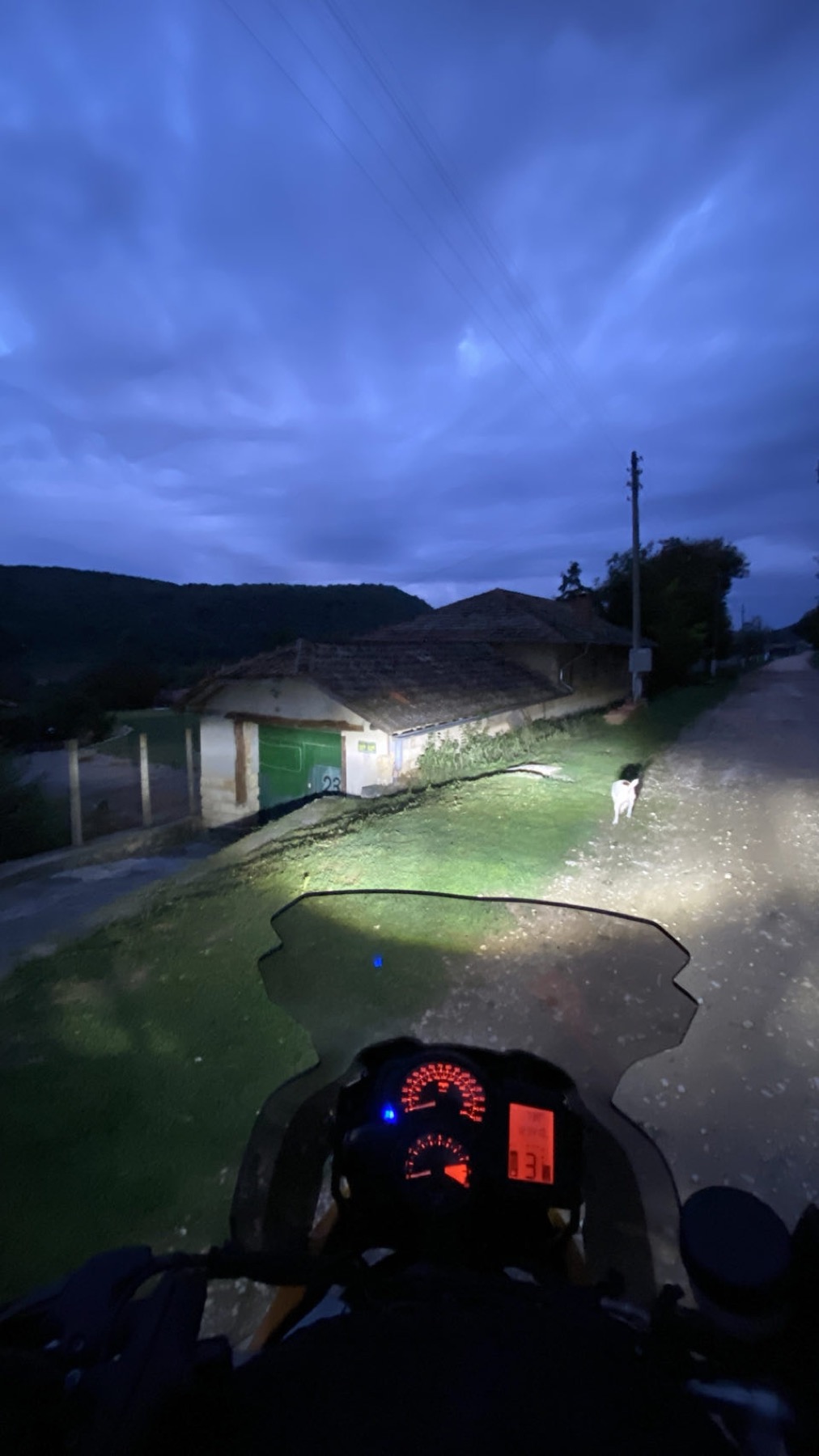 Riding out of a Bulgarian village at dusk, a dog crossing in the headlight