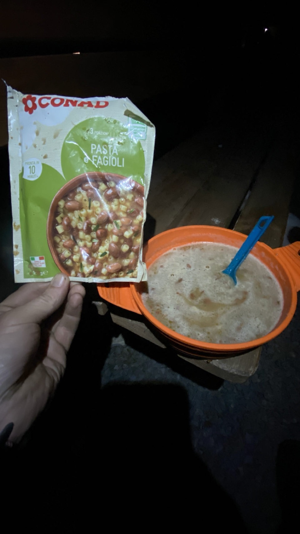 A sachet of pasta e fagioli cooked in a plastic bowl on the ground at night