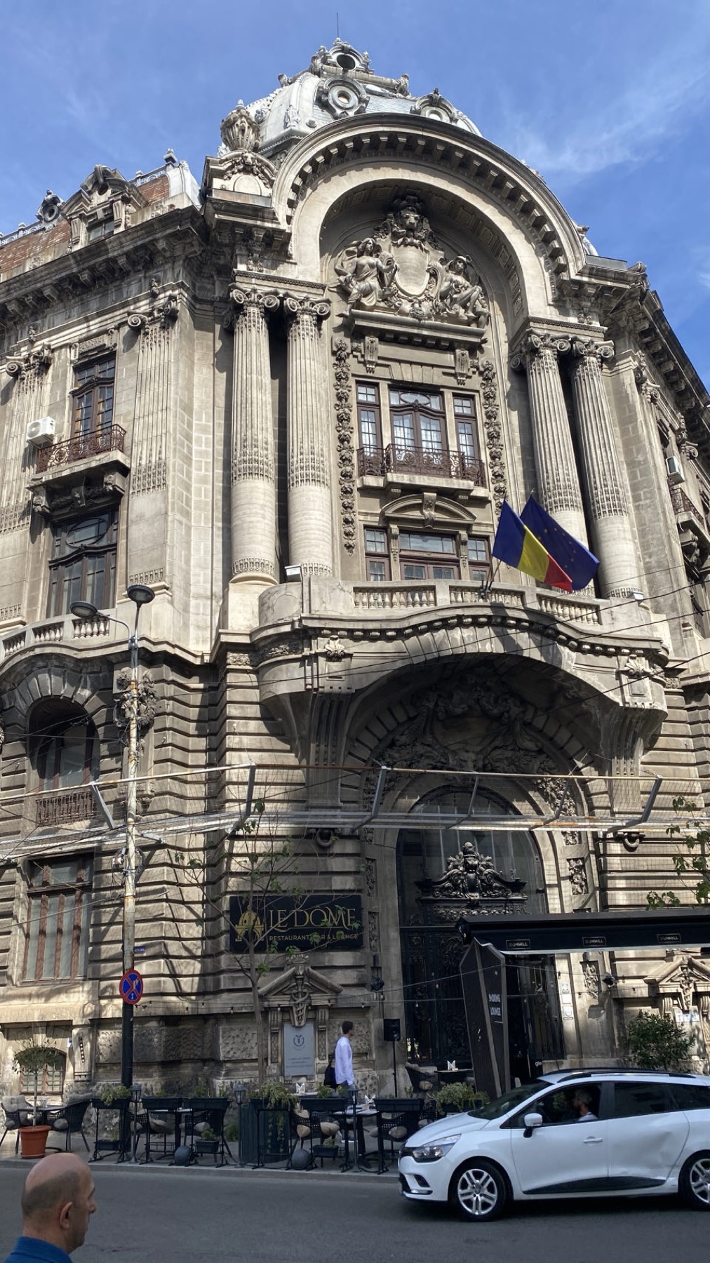 An ornate stone building in Bucharest with Romanian flags on the corner