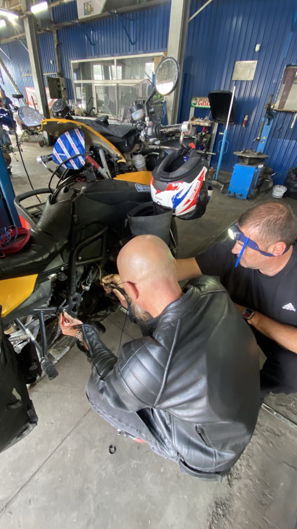 Two mechanics working on the motorcycle in a blue workshop