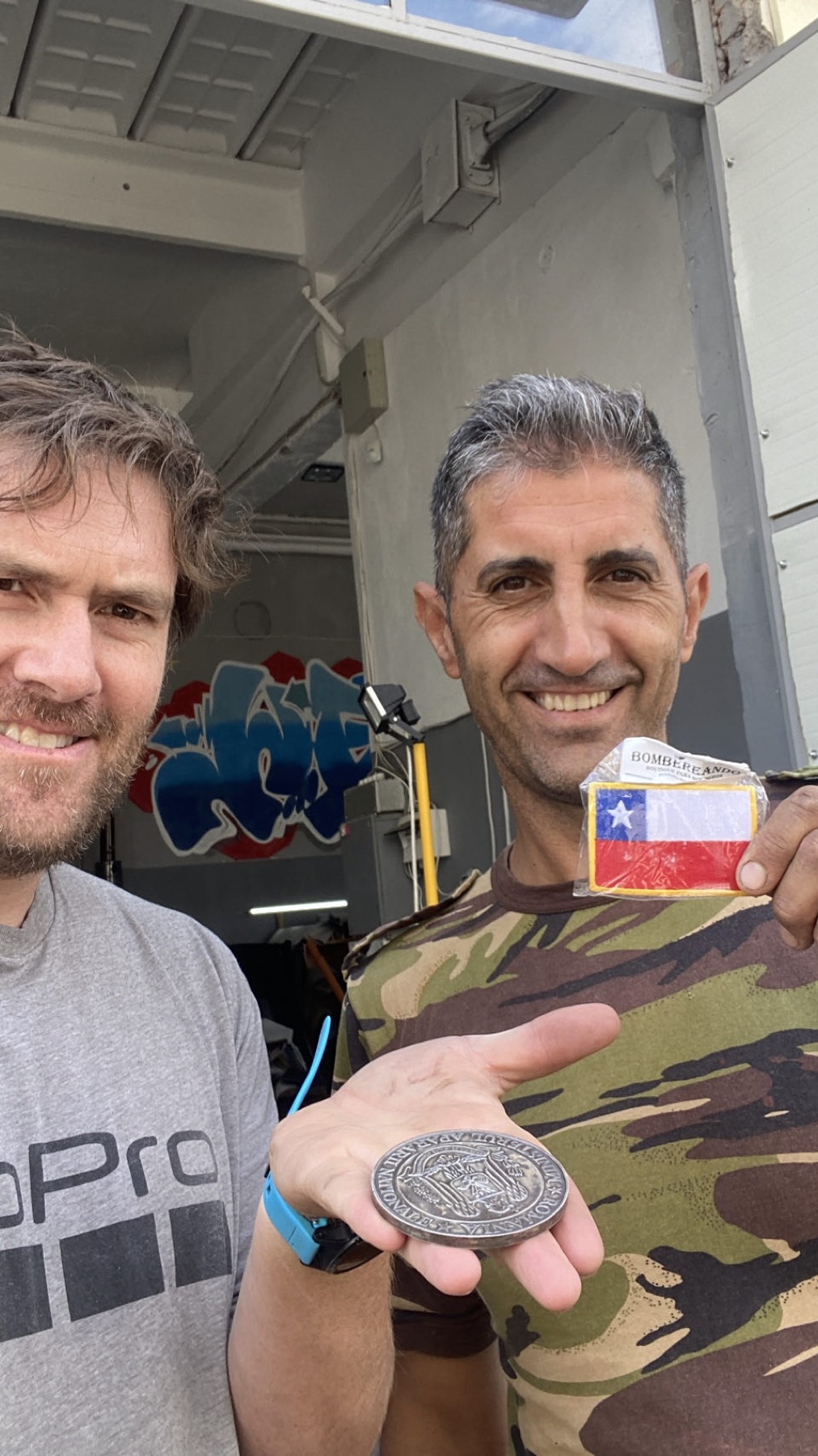 Rodrigo and Gabriel the mechanic holding up a Chilean flag patch and a coin