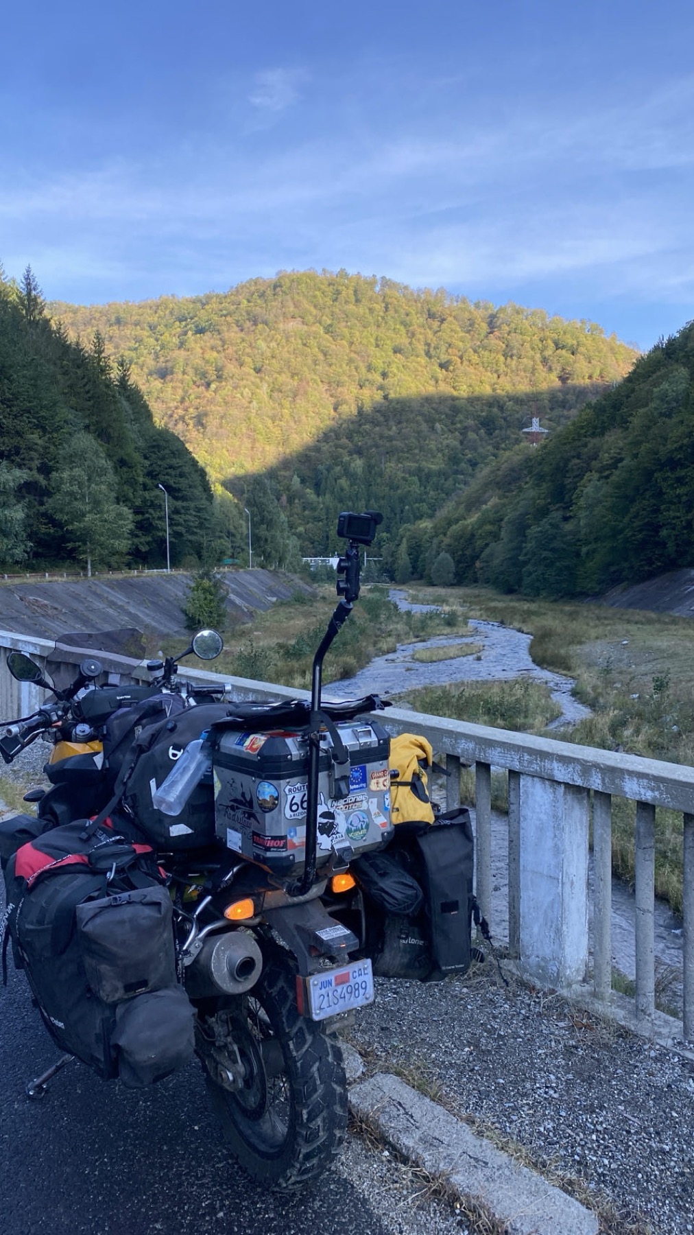 The loaded motorcycle parked on a bridge over a river in a wooded valley