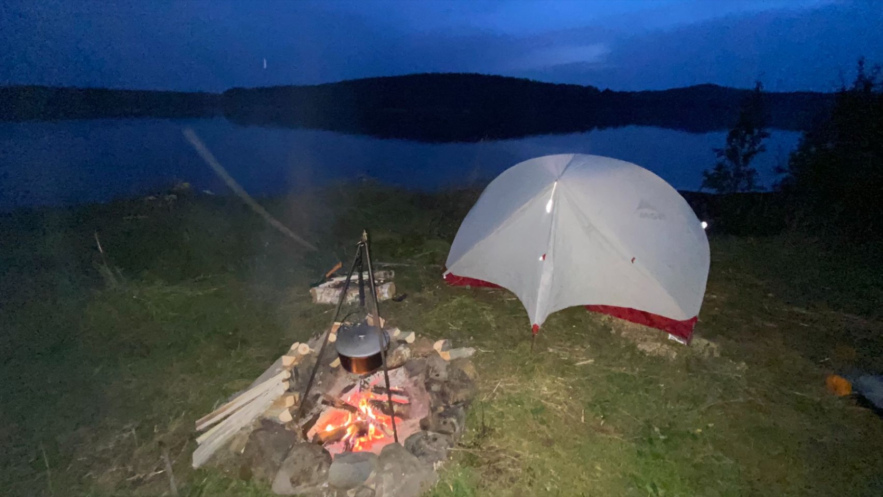 A tent and campfire beside a Karelian lake at dusk