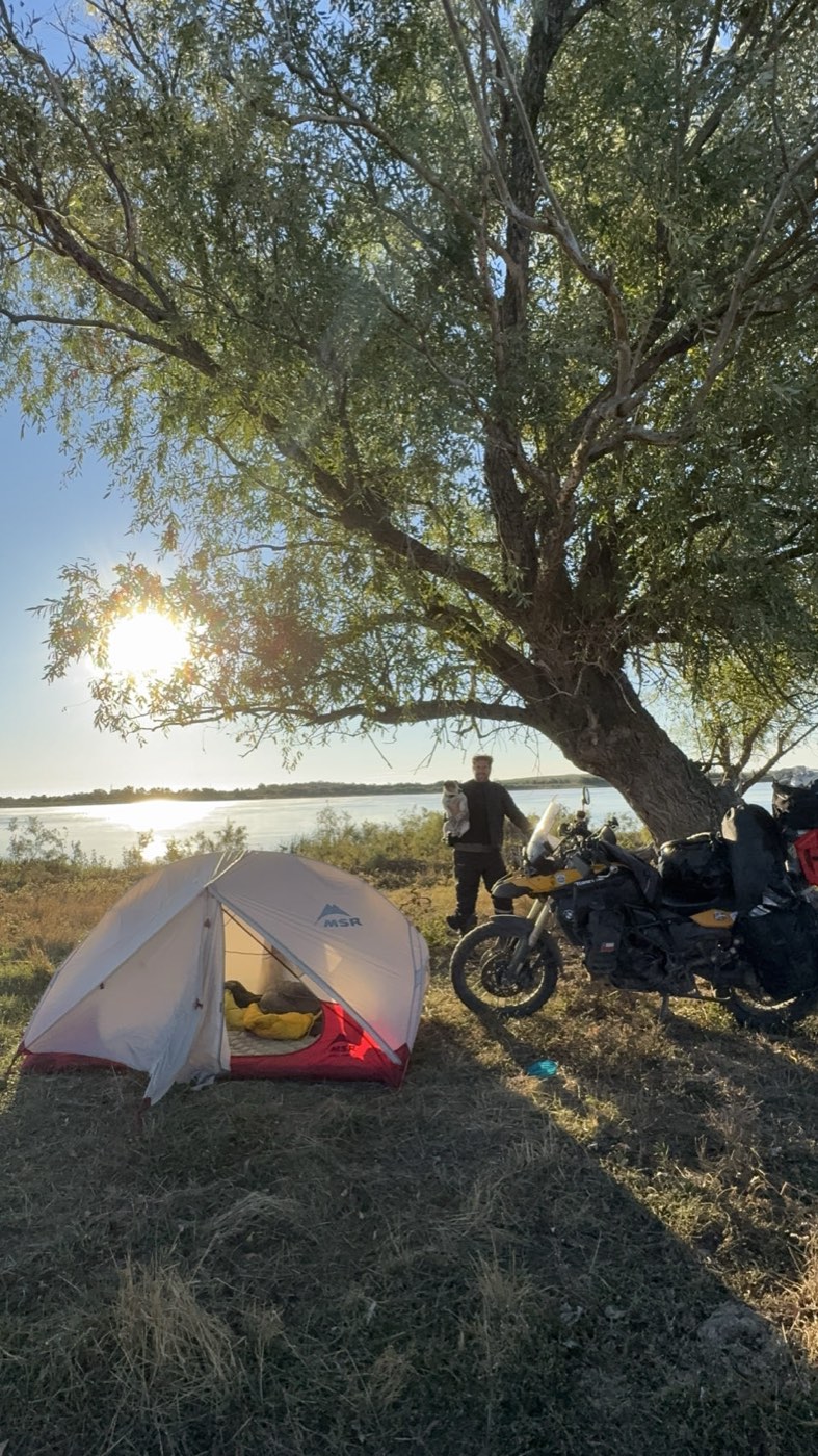 The tent and the motorcycle under a willow on the bank of the Volga at sunrise