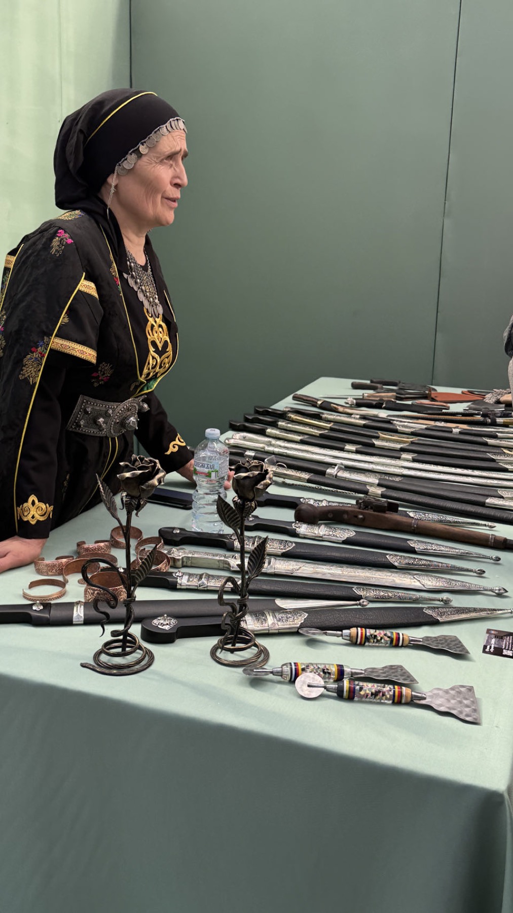 A woman in traditional dress behind a table of daggers