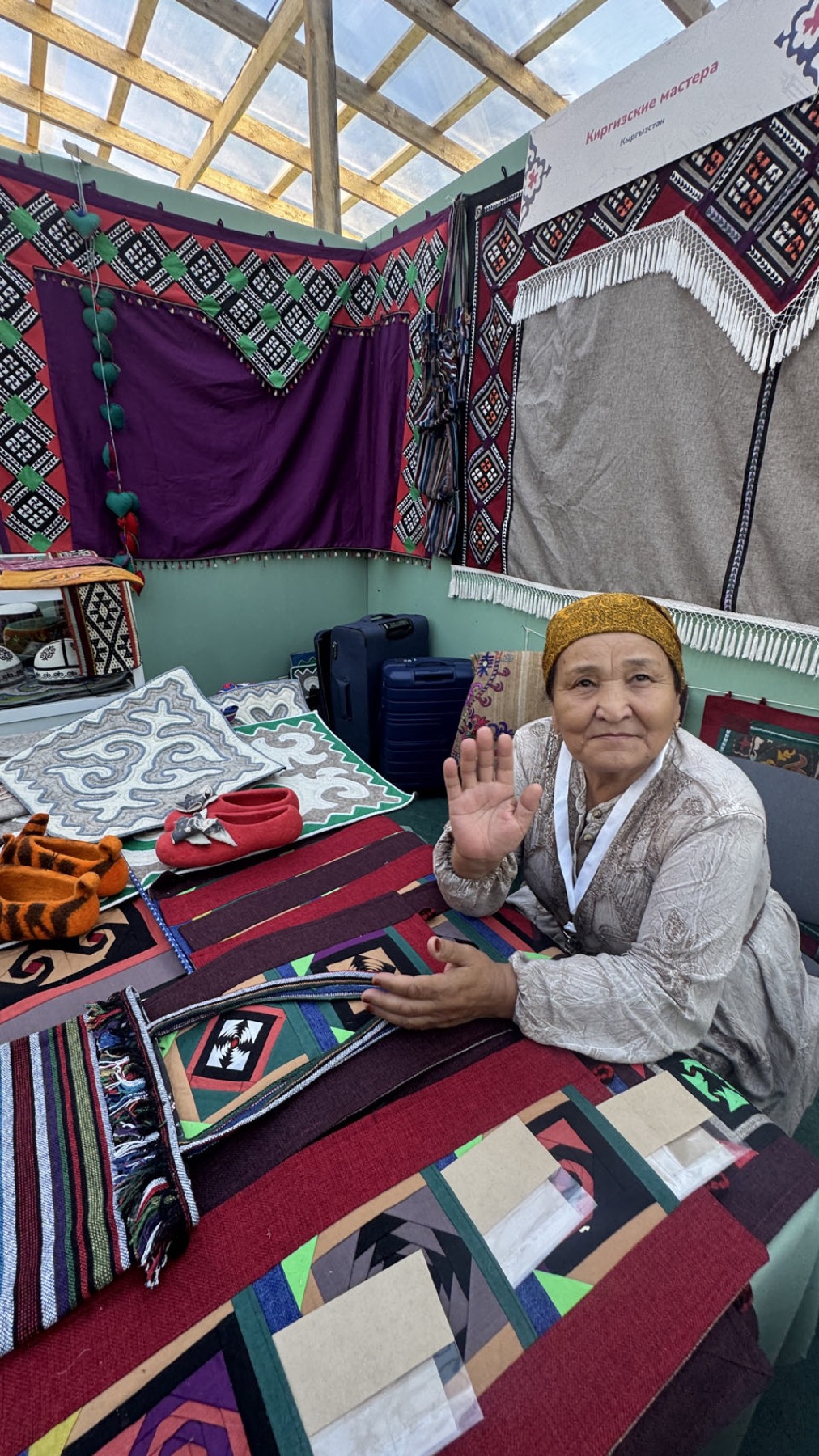 A woman waving from her stand of woven carpets and cushions