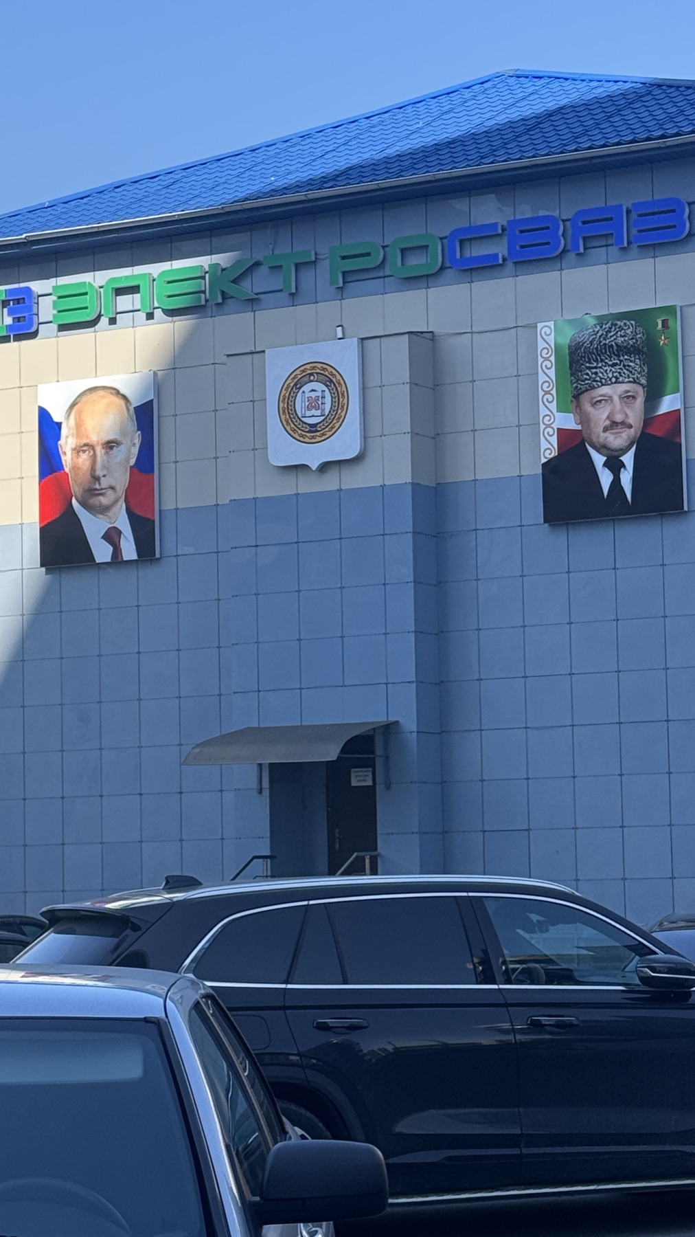 Portraits of Putin and Akhmad Kadyrov mounted on a building facade in Grozny, with the republic crest between them