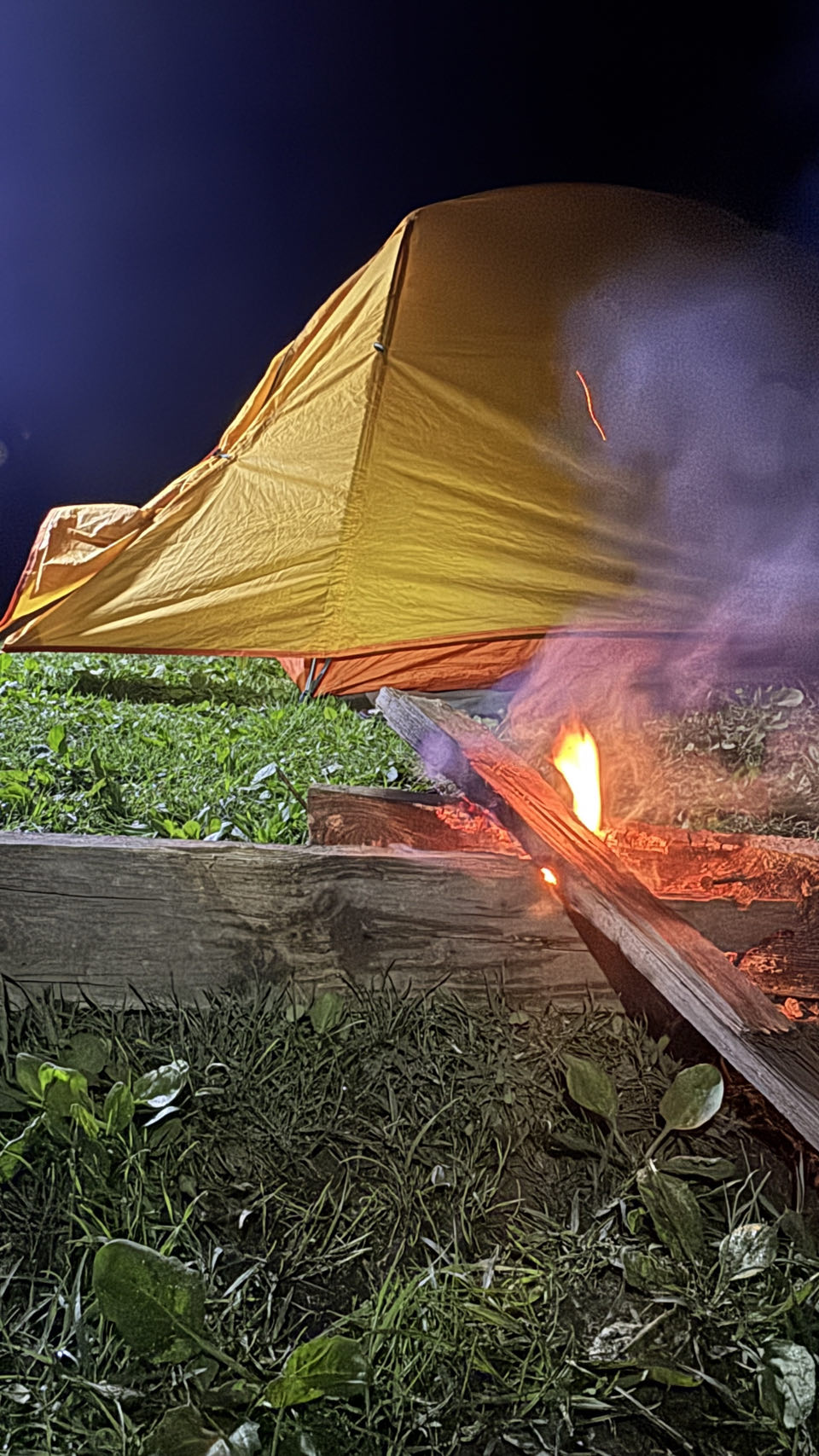 A small fire burning beside the yellow tent at night