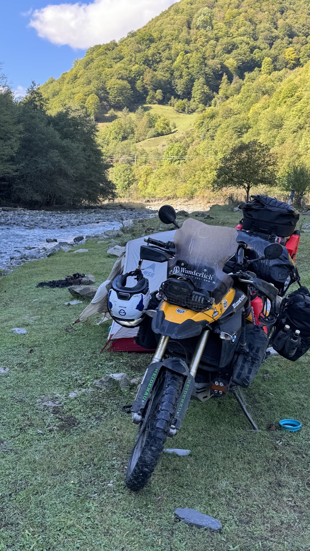 The tent and the loaded motorcycle camped on the grass beside a river below Dusheti