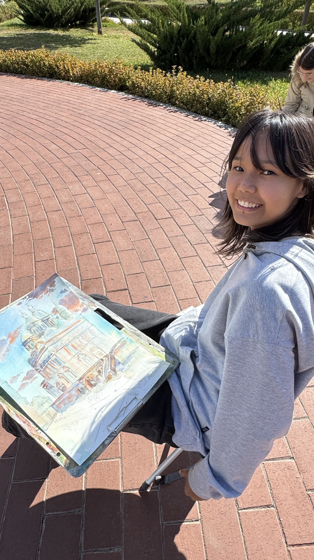 A student sitting outside with a watercolour of the cathedral on her lap