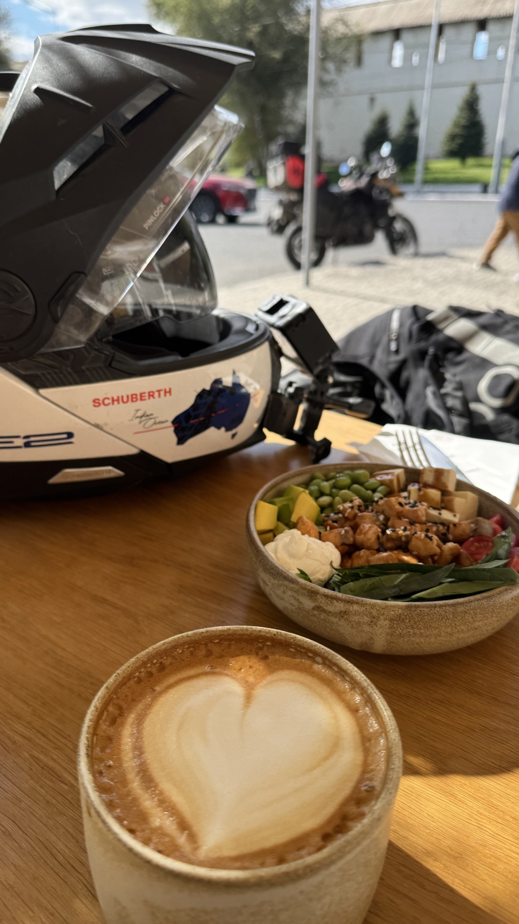 A flat white and a bowl of food on a cafe table, with the helmet beside them and the motorcycle outside the window