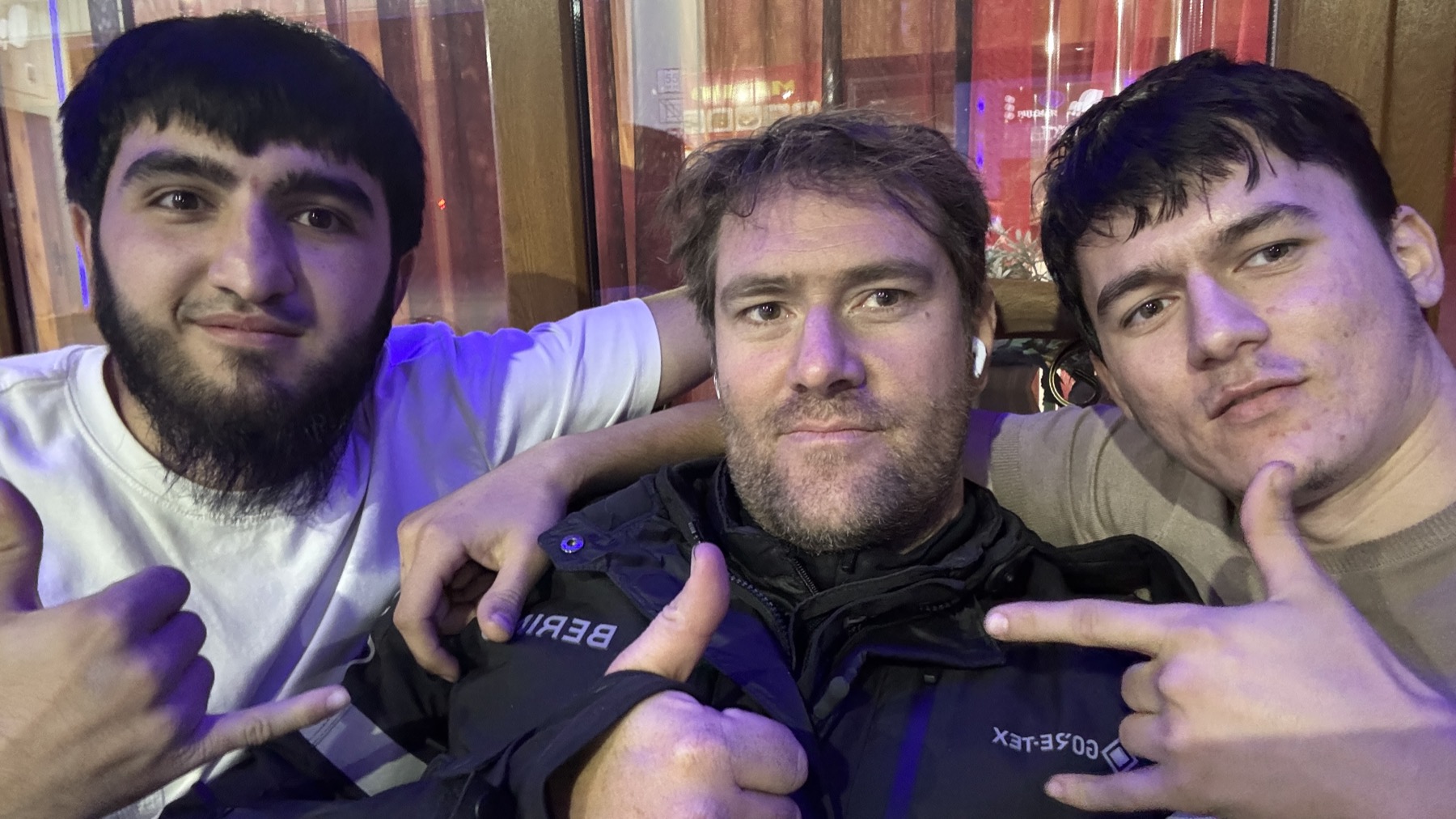 Rodrigo between two young Chechen men in a bar at night, all three of them posing for the camera