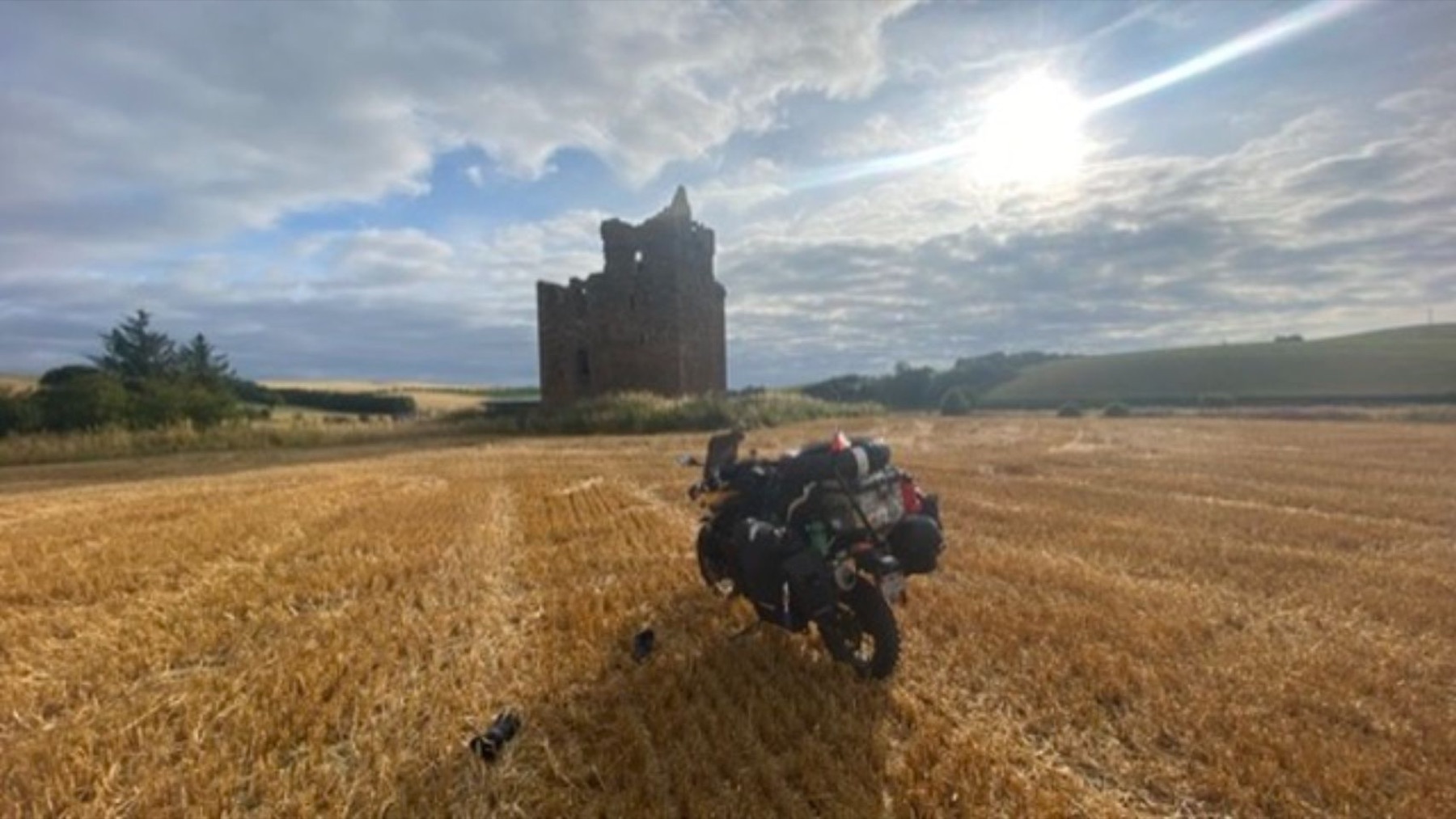 The loaded bike in a wheat field with a stone tower behind it