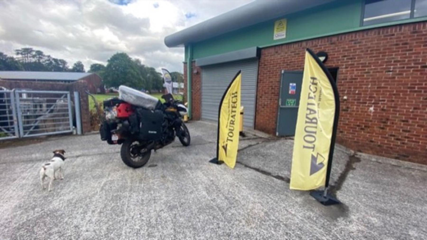 The loaded motorcycle parked between Touratech flags outside the workshop
