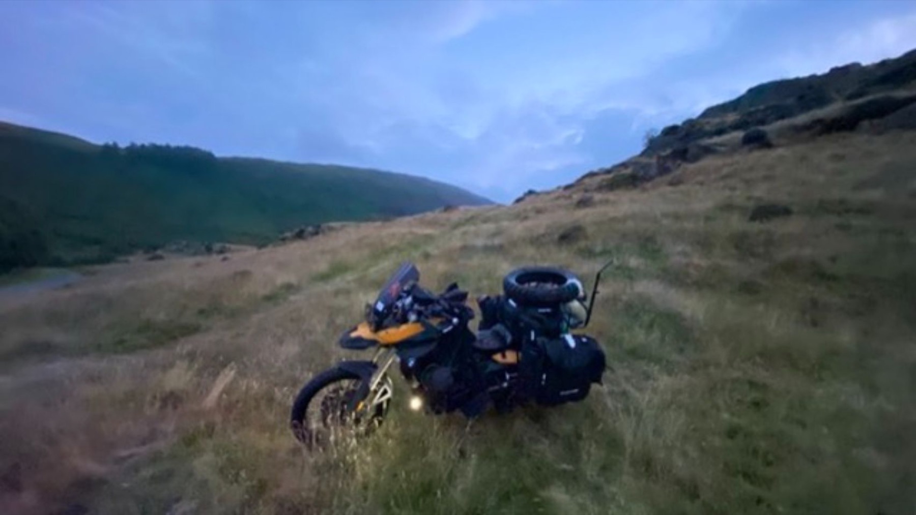 The loaded motorcycle standing in open grass with hills behind
