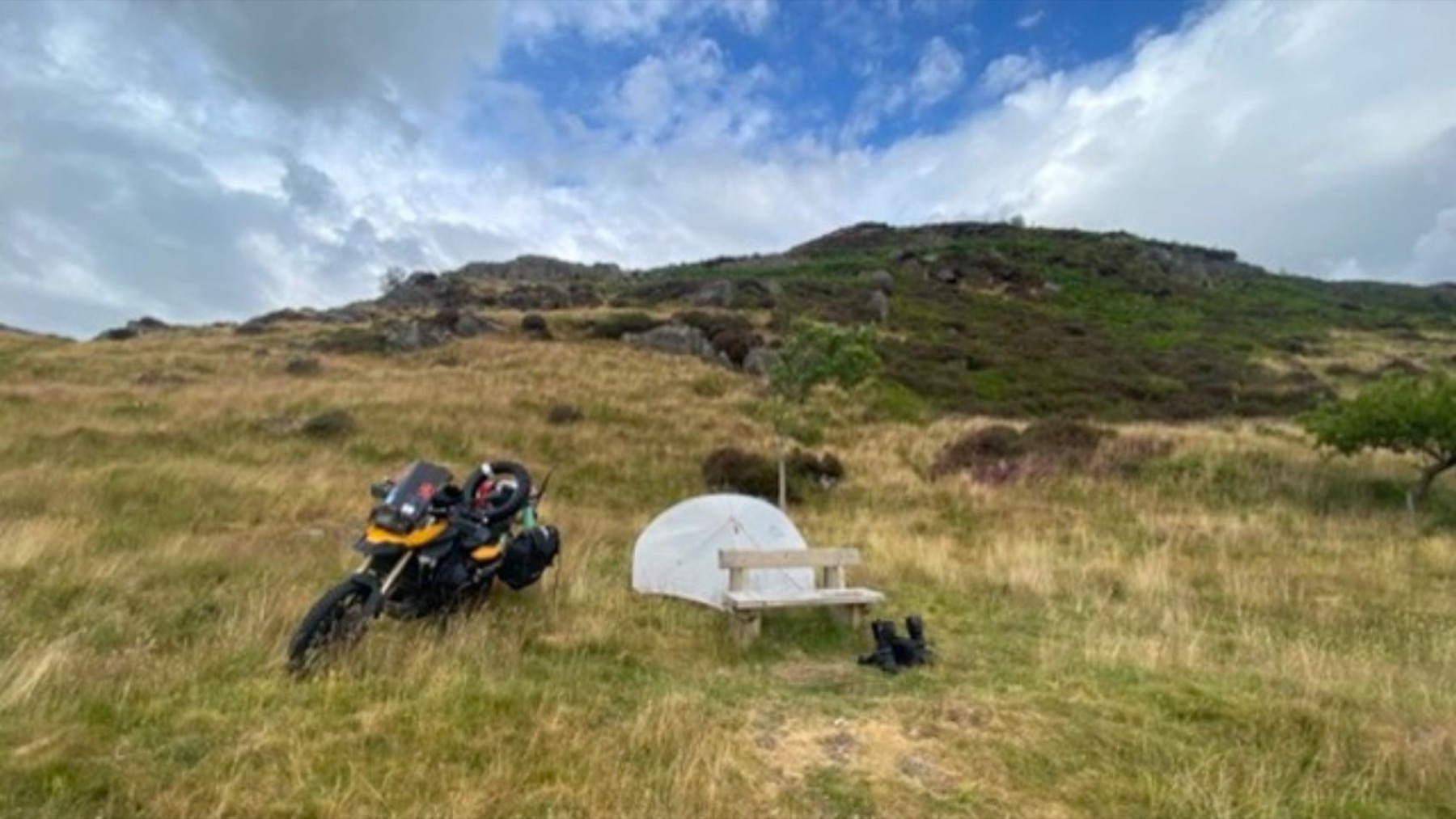 The tent pitched beside the motorcycle in an empty green valley