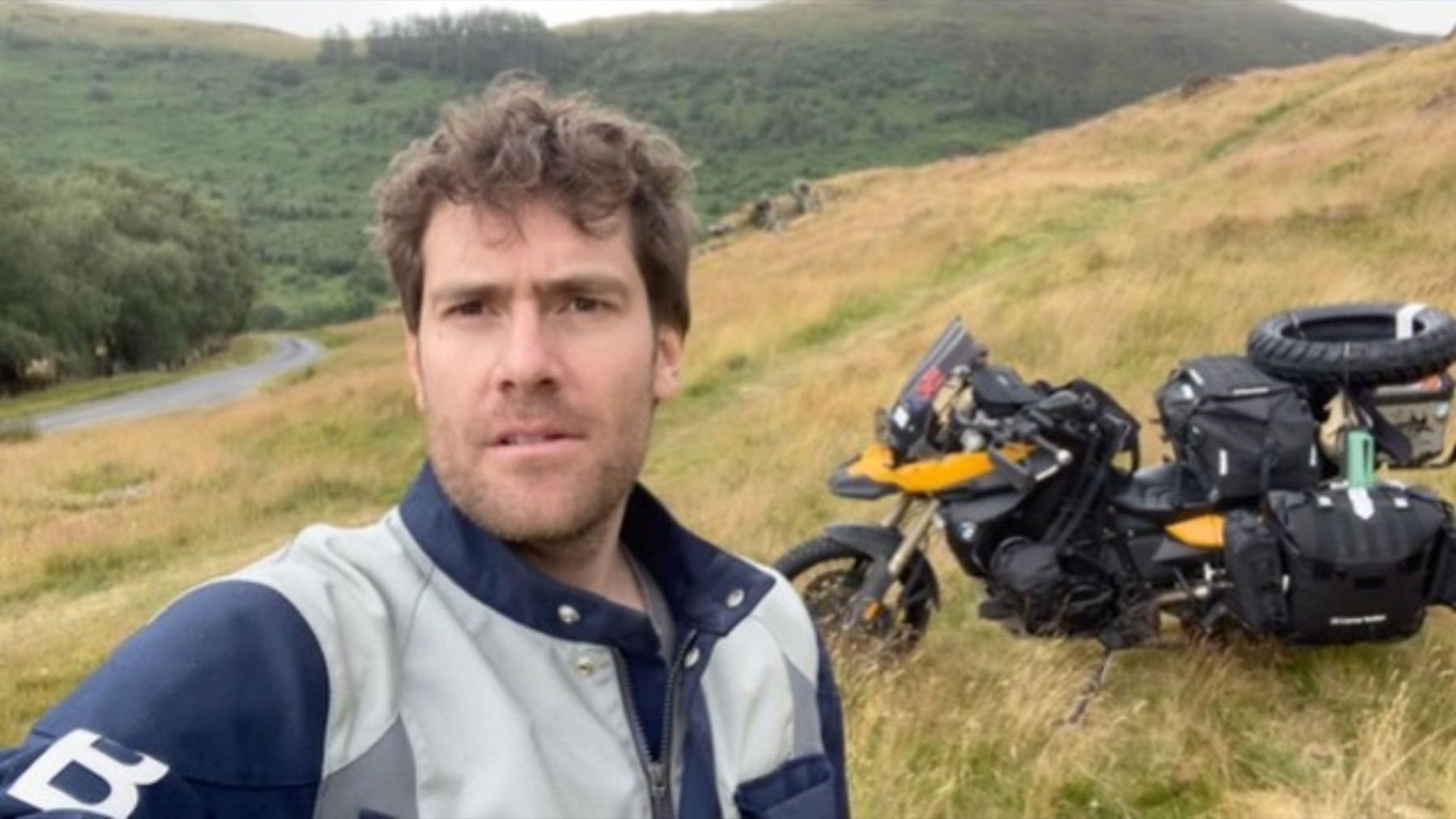 Rodrigo beside the motorcycle in the hills, in riding gear