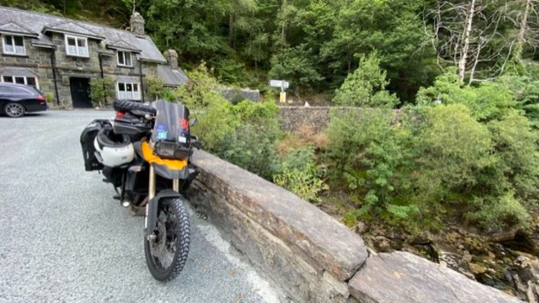 The motorcycle parked on a bridge over a river in the woods